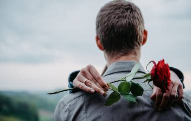 Frau umarmt Mann mit Rose in der Hand