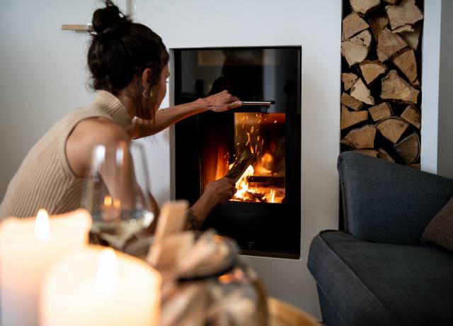 Frau legt Holz in Kamin im Weingarten-Resort Unterlamm Loipersdorf